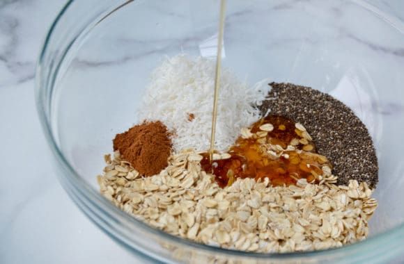 A glass bowl containing oats, coconut, spices and honey