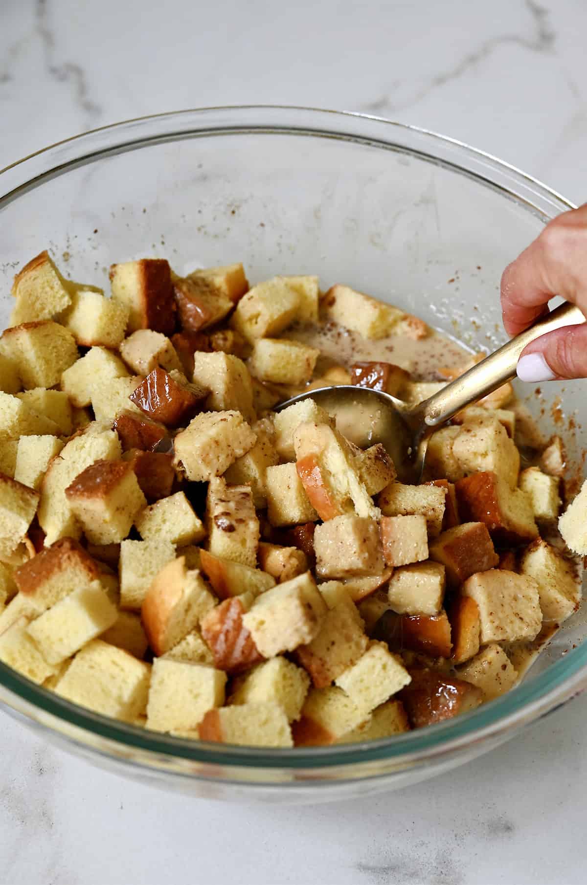 Cubed brioche being mixed with a cinnamon-vanilla custard in a large prep bowl.