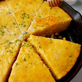 Honey being drizzled on simple skillet cornbread topped with fresh chives