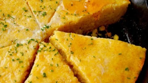 Honey being drizzled on simple skillet cornbread topped with fresh chives