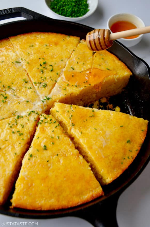 Honey being drizzled on simple skillet cornbread topped with fresh chives