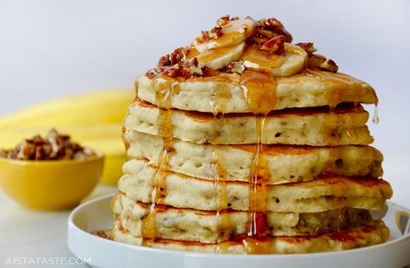 A white plate containing banana nut pancakes topped with syrup