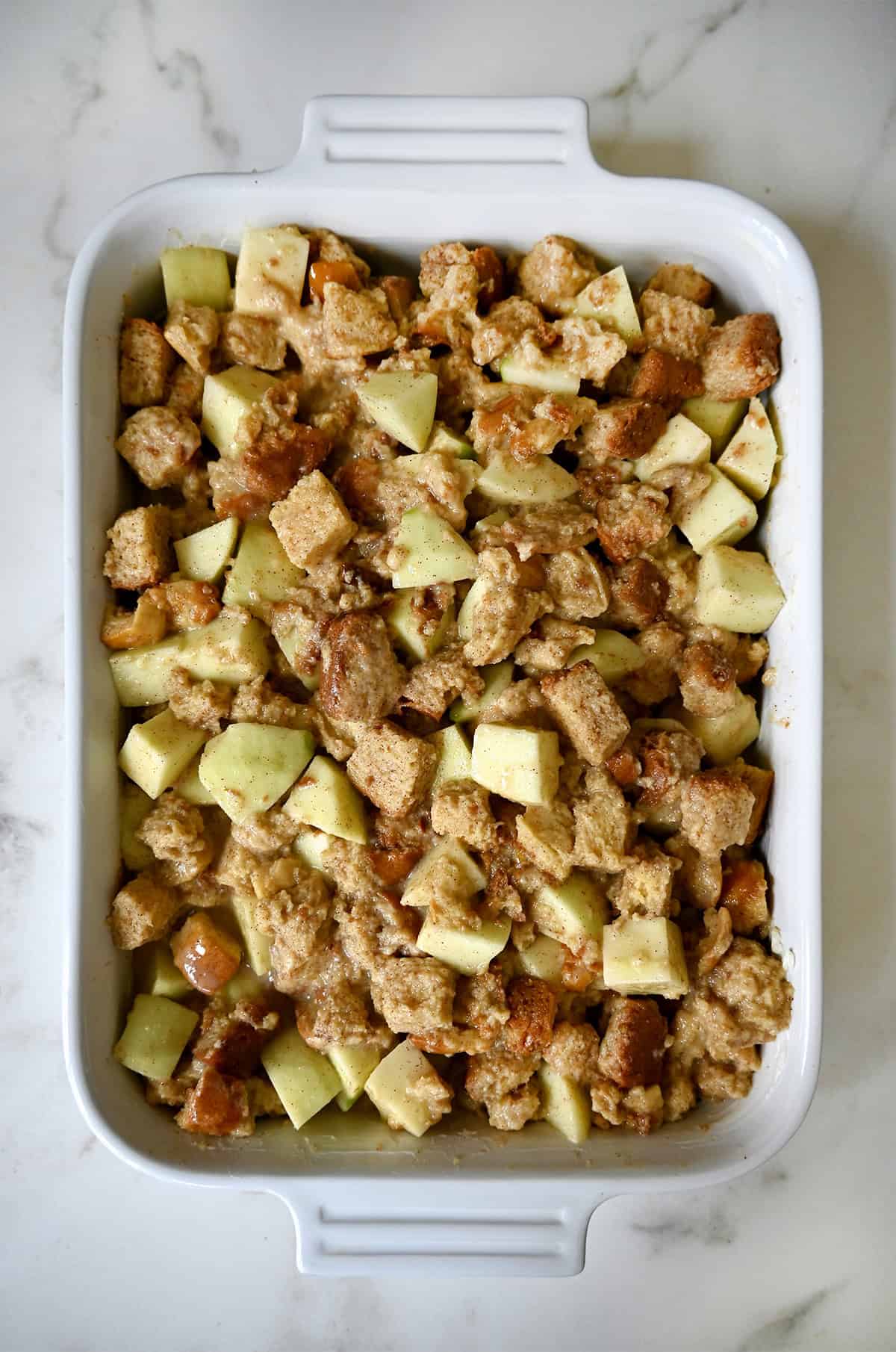 Apple bread pudding with cinnamon custard in a 9x13-inch baking dish before going into the fridge to rest.