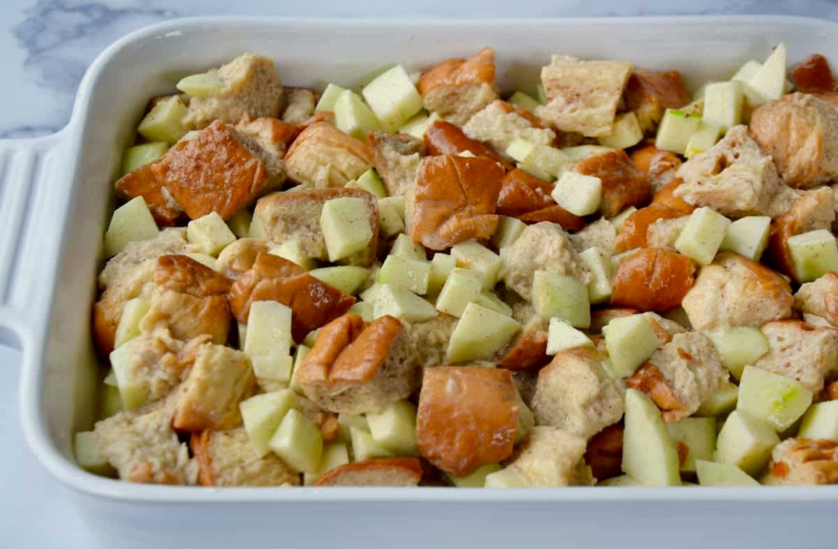 Cubes of brioche bread, chopped apples and a vanilla custard in a baking dish before going into the oven to bake.