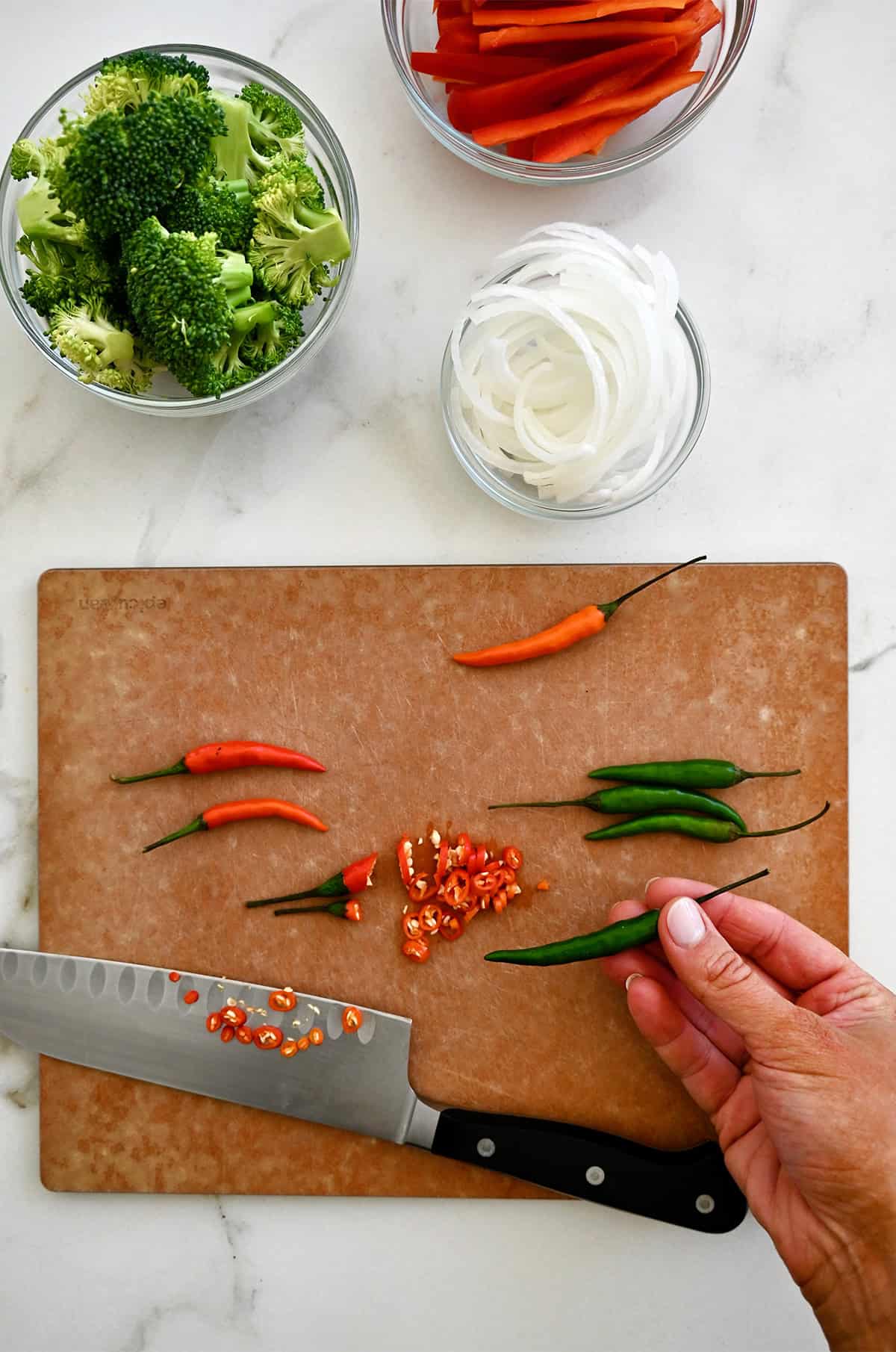 Bird's eye chili peppers on a cutting board with a sharp knife.