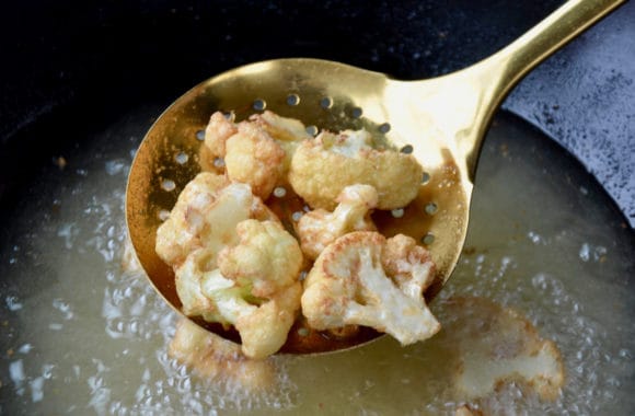 Lightly fried cauliflower florets in slotted spoon over hot oil