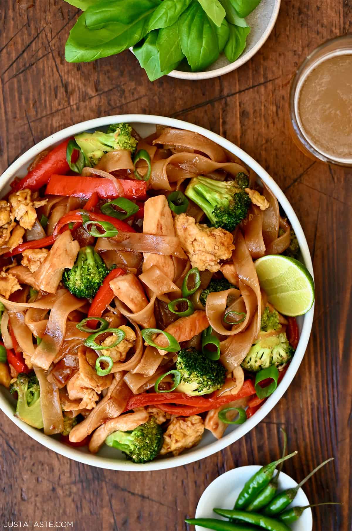 Thai drunken noodles with broccoli, red bell pepper, onion and scrambled eggs garnished with sliced scallions on a plate.