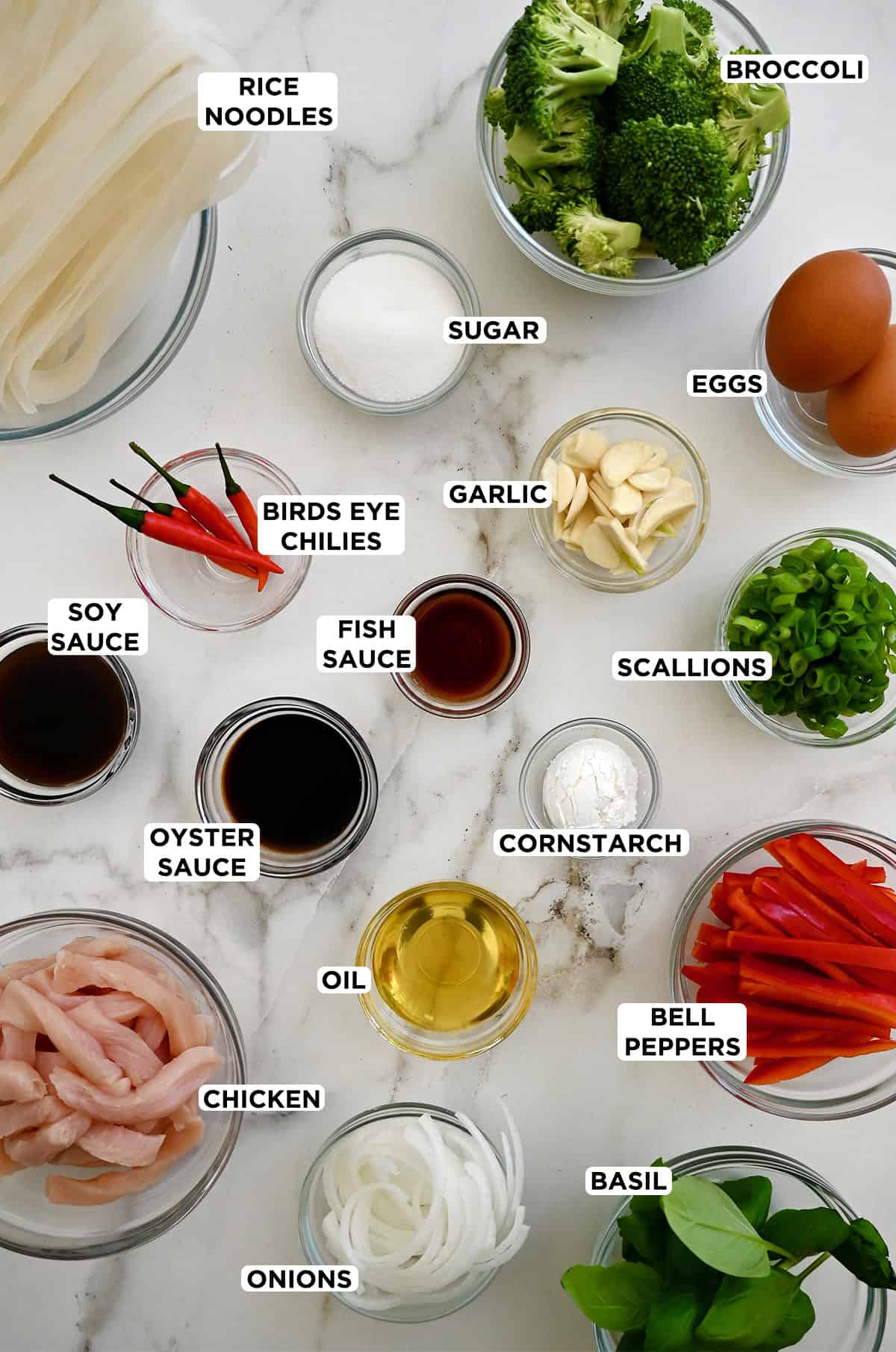 Various sizes of glass bowls containing all of the ingredients needed to make Thai drunken noodles.