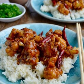 Easy General Tso's Cauliflower over white rice on blue plate with chopsticks