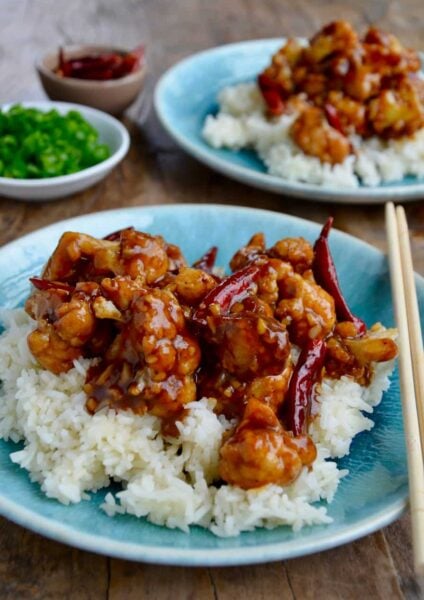 Easy General Tso's Cauliflower over white rice on blue plate with chopsticks
