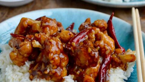 Easy General Tso's Cauliflower over white rice on blue plate with chopsticks