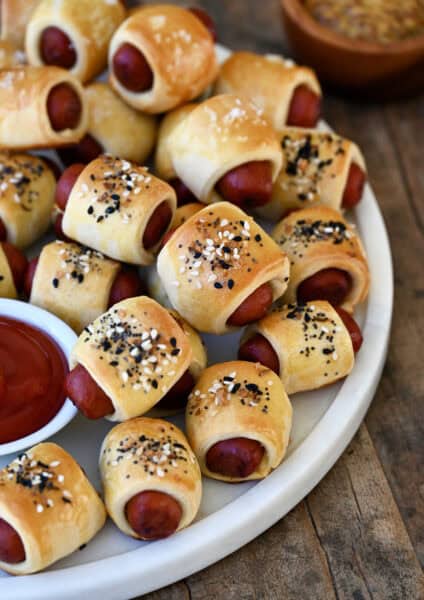 Pigs in a blanket piled on a serving platter with a small bowl containing ketchup.