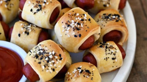 Pigs in a blanket piled on a serving platter with a small bowl containing ketchup.