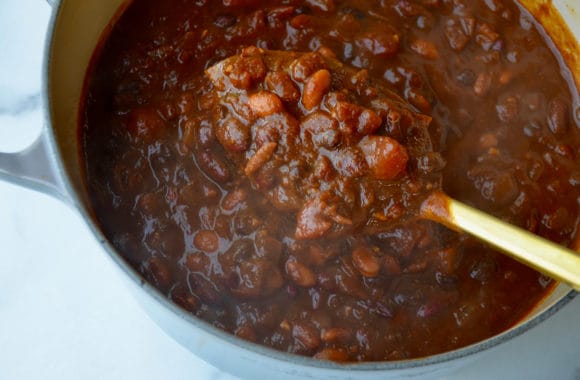 A Dutch oven containing chili being ladled out on a gold spoon