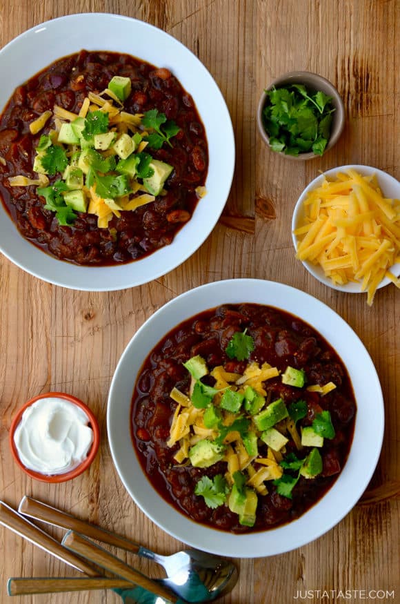 Two white bowls filled with chili and smaller bowls surrounding them containing chili toppings