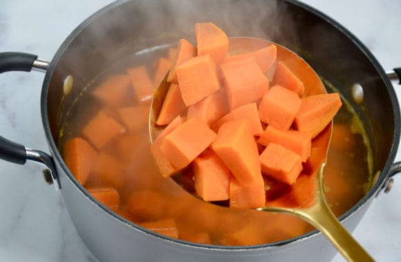 Metal spoon containing diced yams over large stockpot 