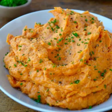 Mashed sweet potatoes garnished with fresh chives in a blue serving bowl.