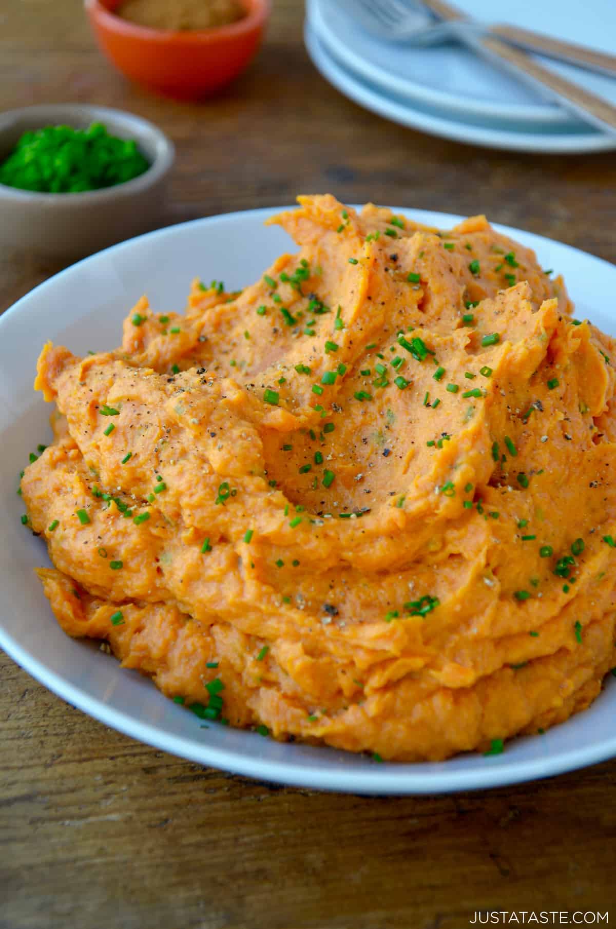 Mashed sweet potatoes garnished with fresh chives in a blue serving bowl.