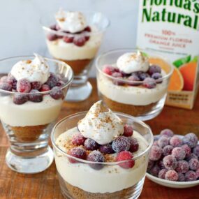 Glass parfait glasses filled with cheese and a carton of orange juice in the background