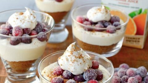 Glass parfait glasses filled with cheese and a carton of orange juice in the background