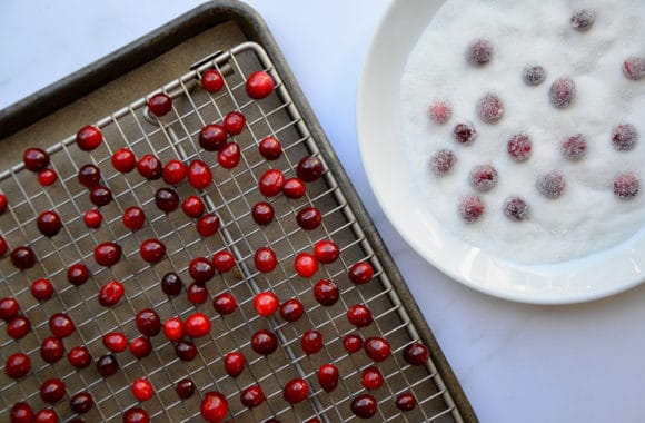 Sugared cranberries on a baking rack and a plate of sugar next to it
