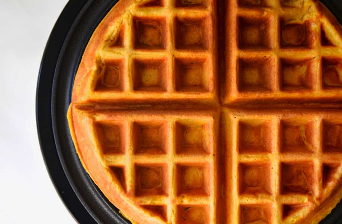 A cooked pumpkin spice waffle is on the cooking surface of a waffle baker.