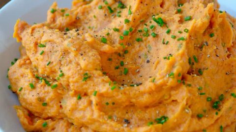 A serving bowl containing The Best Mashed Sweet Potatoes topped with fresh minced chives