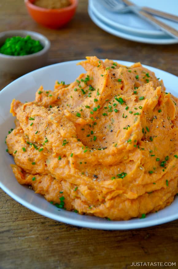 A serving bowl containing The Best Mashed Sweet Potatoes topped with fresh minced chives