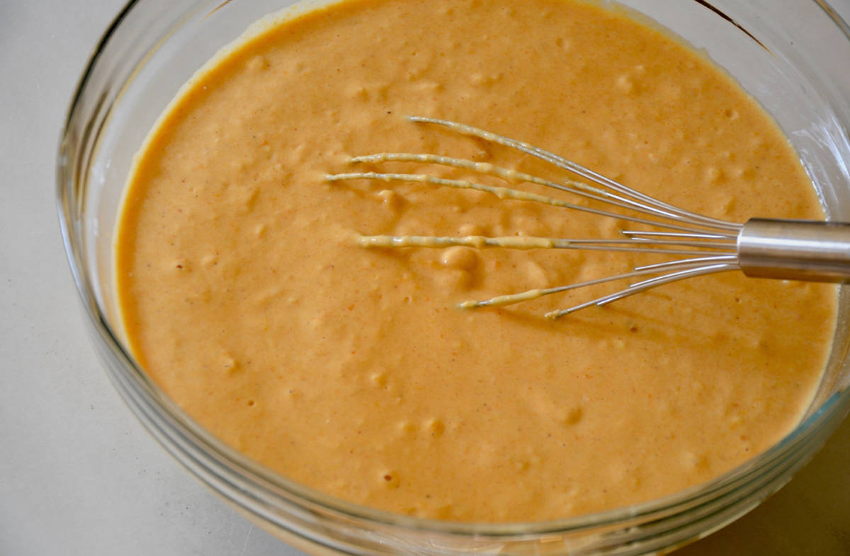 A clear bowl contains pumpkin waffle batter and a whisk.