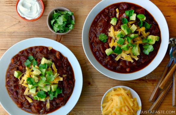 Two bowls of chili surrounded by cilantro, cheese and sour cream