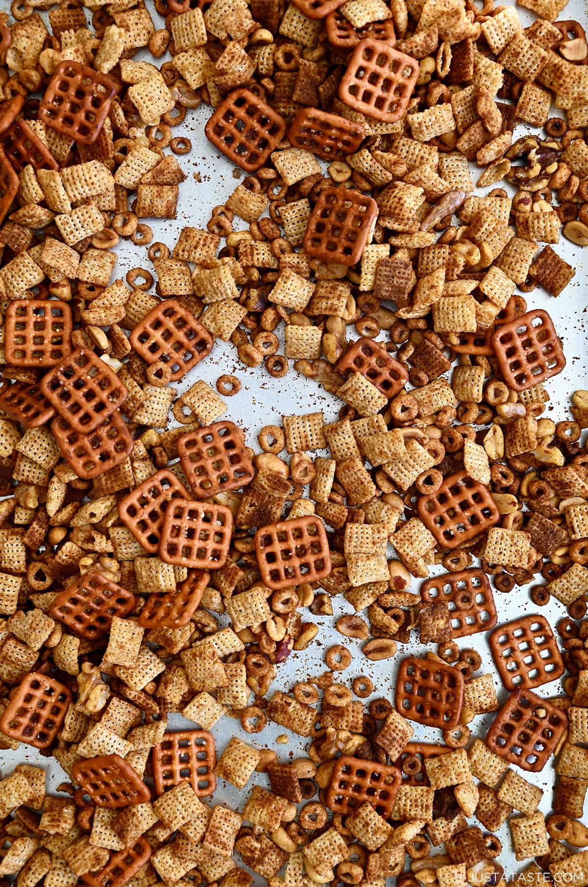 Homemade Chex Mix with pretzels, peanuts, halved walnuts and Cheerios on a metal baking sheet.