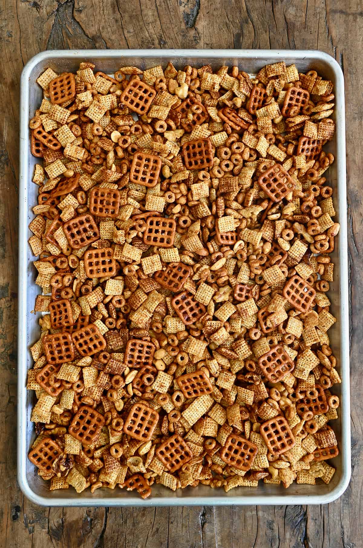 Chex party mix with Cheerios, nuts and pretzels, cooling on a baking sheet.