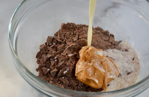 Heavy cream being poured into bowl containing chopped chocolate and creamy peanut butter