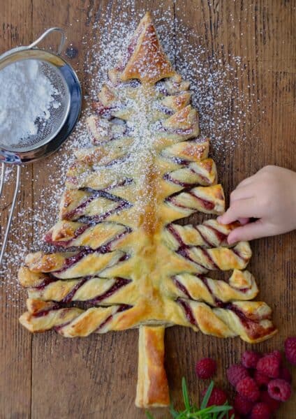 Child's hand reaching for a Christmas Tree Puff Pastry sprinkled with confectioners' sugar.