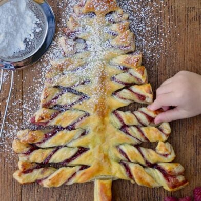 Child's hand reaching for a Christmas Tree Puff Pastry sprinkled with confectioners' sugar