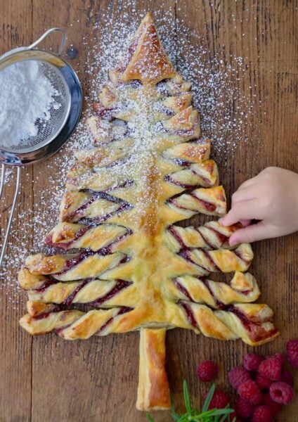 Child's hand reaching for a Christmas Tree Puff Pastry sprinkled with confectioners' sugar
