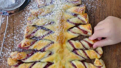 Child's hand reaching for a Christmas Tree Puff Pastry sprinkled with confectioners' sugar