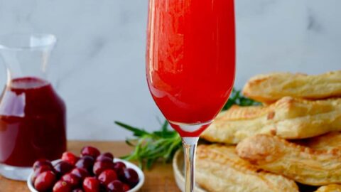 Cranberry Champagne Cocktail in Champagne flute with orange twist and fresh cranberries and pastries in the background