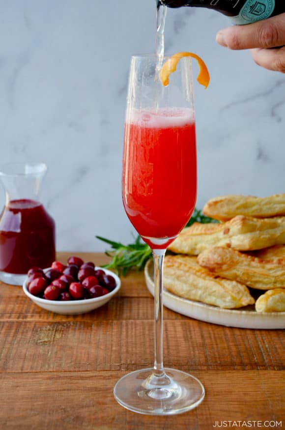 Cranberry Champagne Cocktail in Champagne flute with orange twist and fresh cranberries and pastries in the background