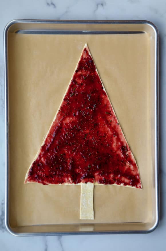 Jam spread over tree-shaped puff pastry on parchment paper lined baking sheet