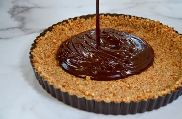 Chocolate mixture being poured into pretzel tart shell