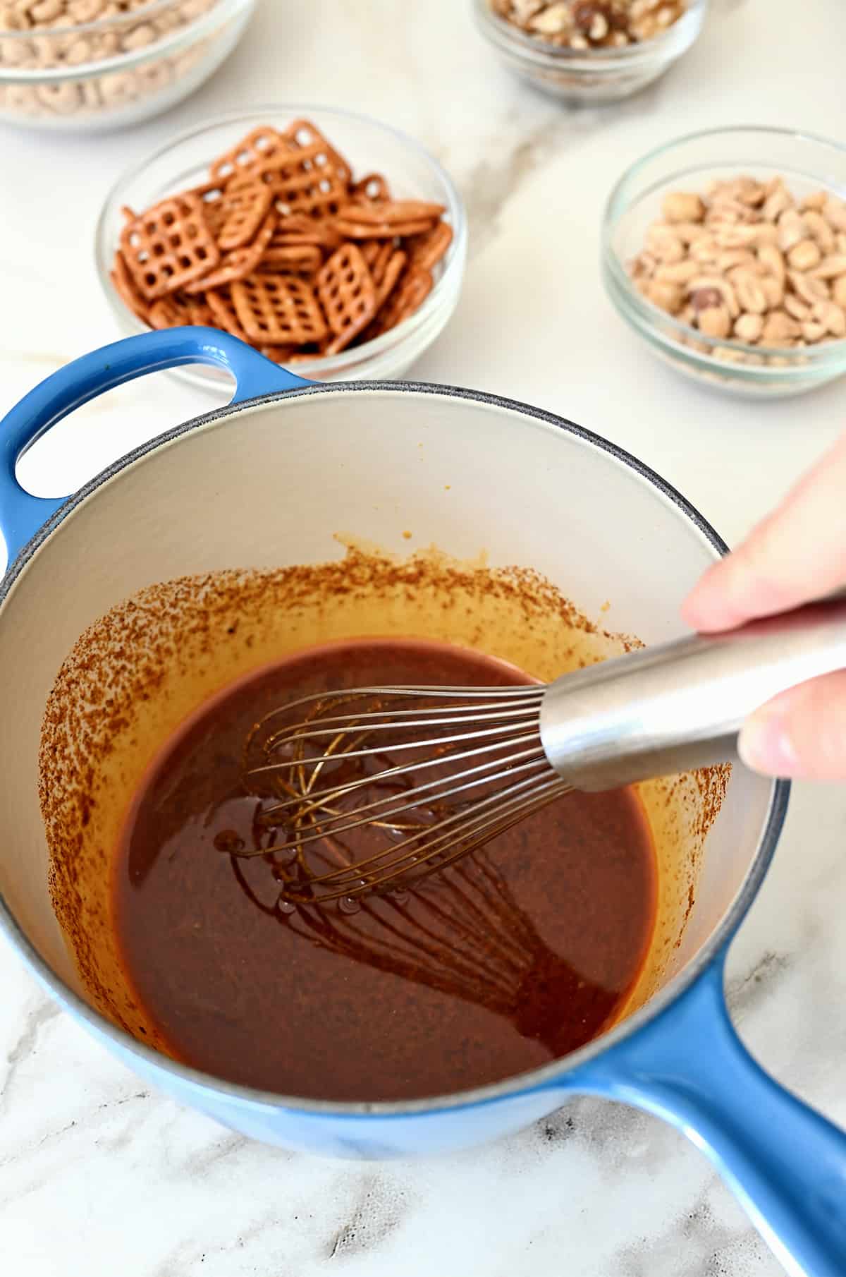 A hand holding a whisk mixes a seasoned sauce in a small saucepan.