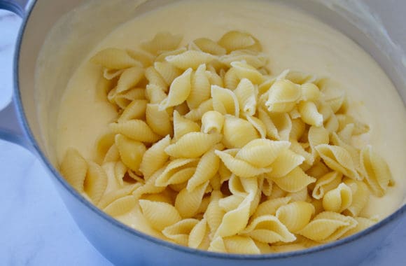 A Dutch oven filled with bechamel cheese sauce and shell pasta