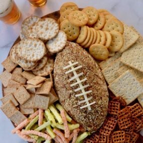 A wood board with a football cheese ball and snack foods surrounding it