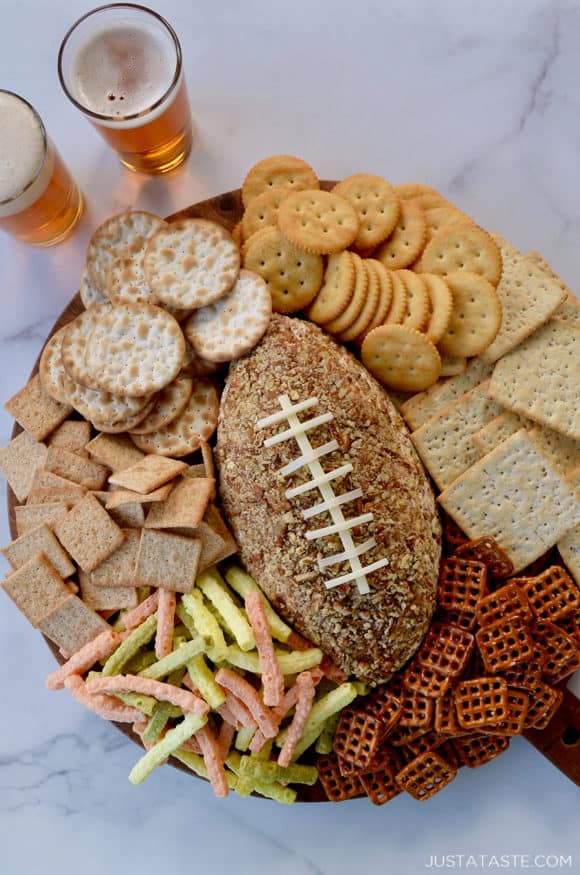 A wood board with a football cheese ball and snack foods surrounding it