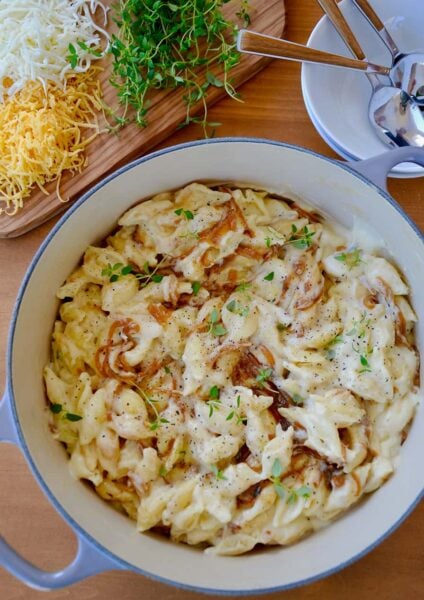 A pot of mac and cheese with caramelized onions and small bowls surrounding it