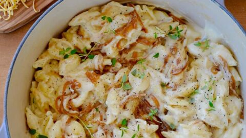 A pot of mac and cheese with caramelized onions and small bowls surrounding it