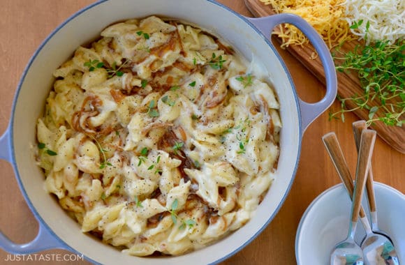 A pot with mac and cheese surrounded by shredded cheese and fresh thyme