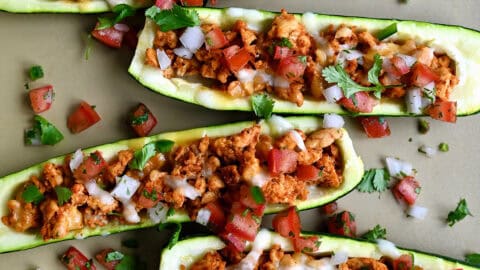Healthy Zucchini Boats filled with taco-seasoned ground turkey, cheese, and topped with fresh cilantro and pico de gallo on a baking sheet.