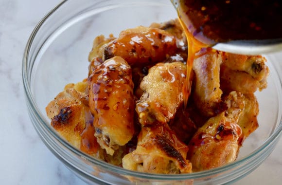 A glass bowl with chicken wings and sauce being poured on top